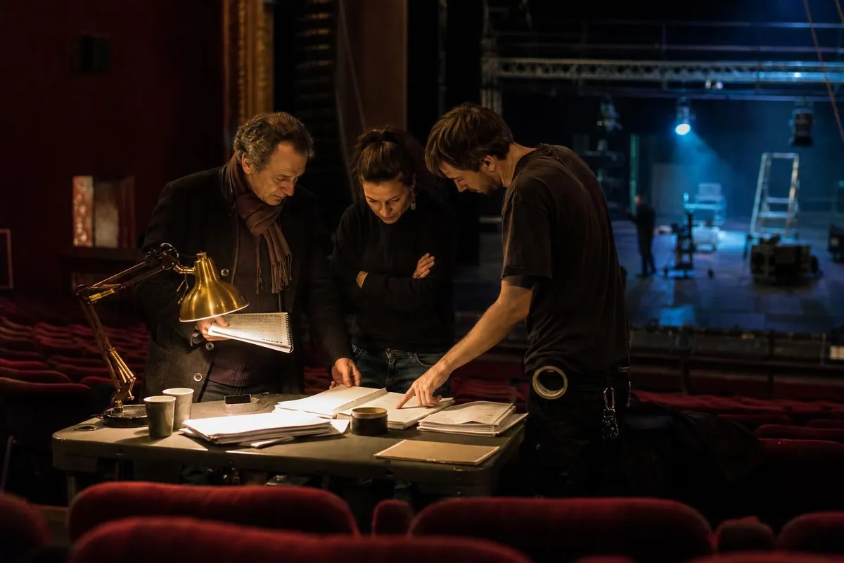 Trois professionnels du spectacle vivant en discussion autour d’une table de régie encombrée de papiers, au fond d’une salle en cours de montage